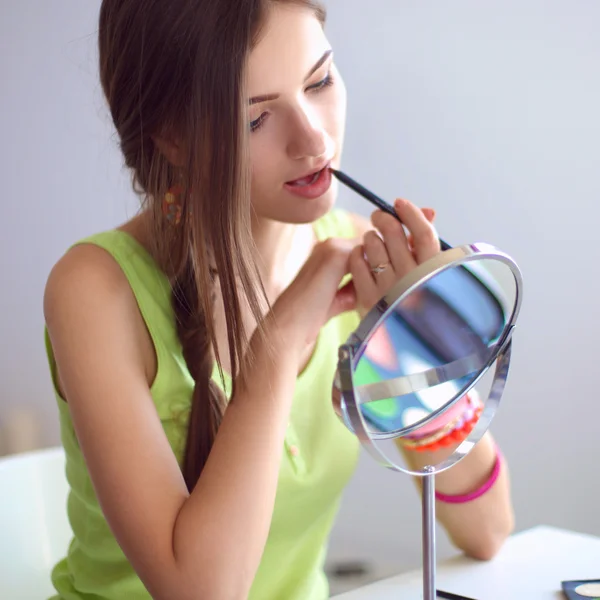 Jeune belle femme se maquillant près du miroir, assise au bureau — Photo