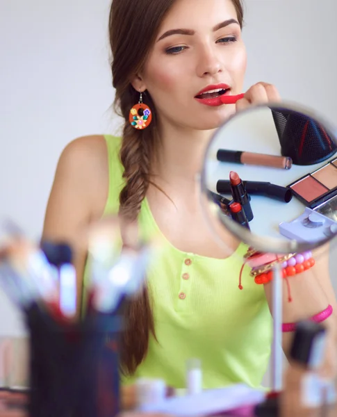 Jeune belle femme se maquillant près du miroir, assise au bureau — Photo