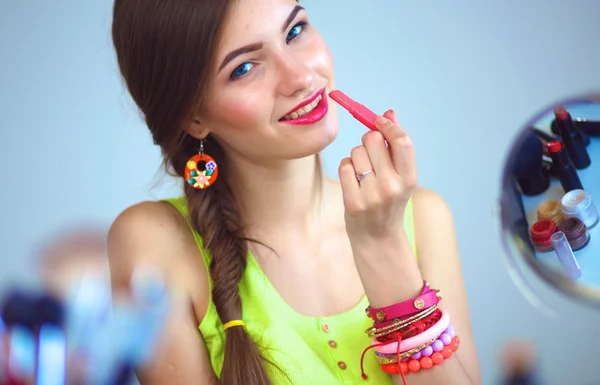 Joven hermosa mujer haciendo maquillaje cerca del espejo, sentado en el escritorio — Foto de Stock