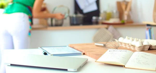 Feliz hermosa mujer de pie en su cocina escribiendo en un cuaderno en casa — Foto de Stock