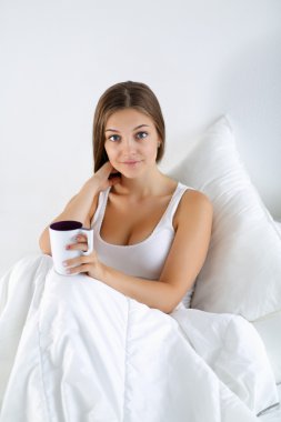 Genç ve güzel bir kadın yatakta çay keyfi