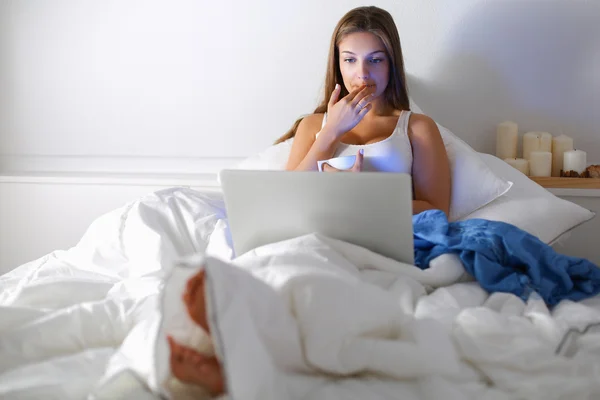 Yatak ve çay tadını çıkarırken bir dizüstü bilgisayar ile genç ve güzel bir kadın — Stok fotoğraf