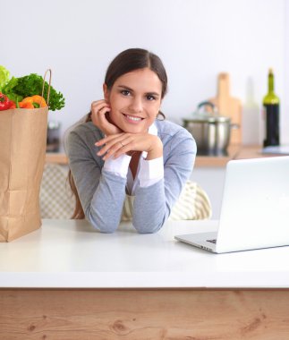 Güzel genç bayan yemek pişiriyor. Mutfakta makbuzu olan dizüstü bilgisayara bakıyor.