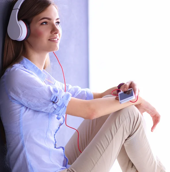 Smiling girl with headphones sitting on the floor near wall — Stock Photo, Image