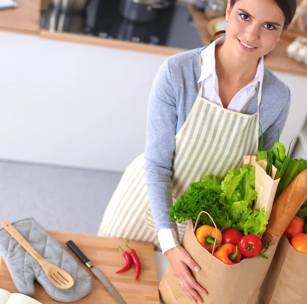 Mutfakta alışveriş torbaları olan bir kadın, masanın yanında duruyor. — Stok fotoğraf