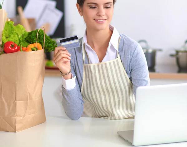 Uśmiechnięta kobieta zakupy online przy użyciu komputera i karty kredytowej w kuchni — Zdjęcie stockowe