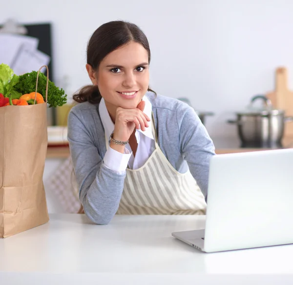 Hermosa joven cocina mirando a la pantalla del ordenador portátil con recibo en la cocina — Foto de Stock