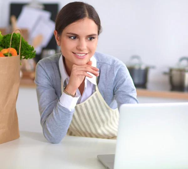 Hermosa joven cocina mirando a la pantalla del ordenador portátil con recibo en la cocina — Foto de Stock