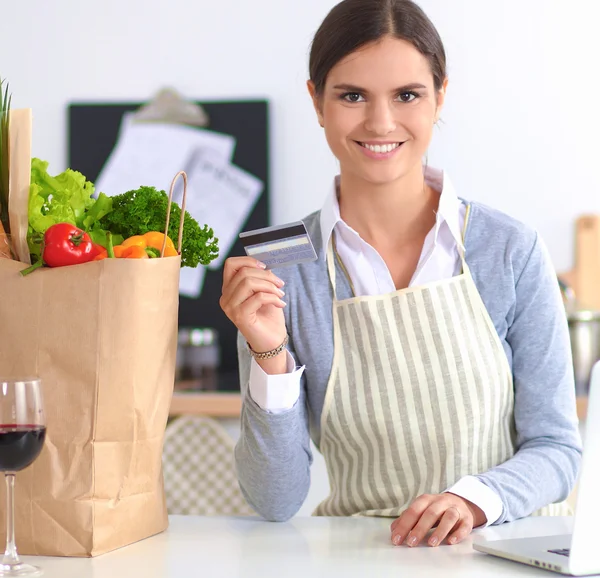 Lachende vrouw online winkelen met behulp van computer en creditcard in de keuken — Stockfoto