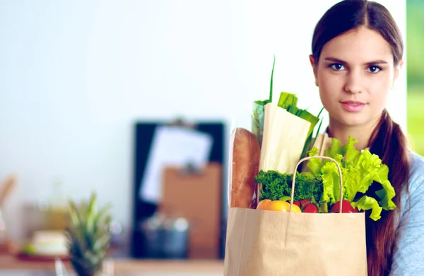 Sebzeli alışveriş poşeti taşıyan genç bir kadın. Mutfakta duruyor. — Stok fotoğraf