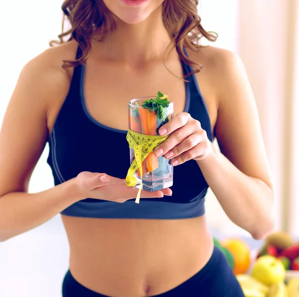 Mujer sosteniendo un vaso lleno de ensalada de frutas frescas con una cinta métrica alrededor del vaso —  Fotos de Stock