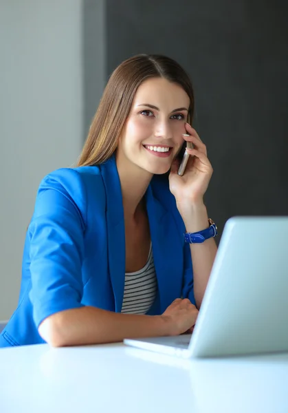 Porträtt av en ung kvinna på telefon framför en bärbar dator. — Stockfoto