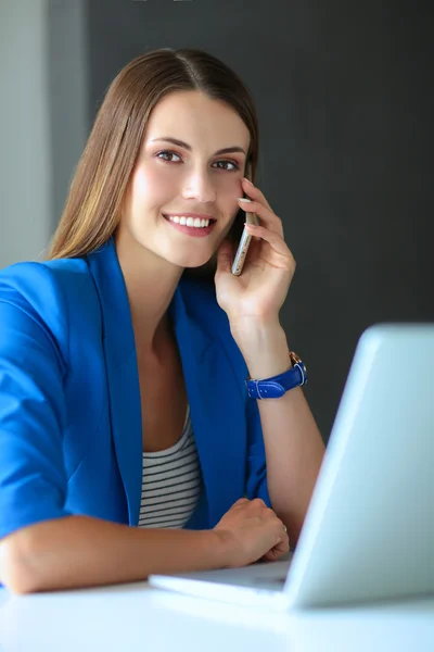 Porträtt av en ung kvinna på telefon framför en bärbar dator. — Stockfoto