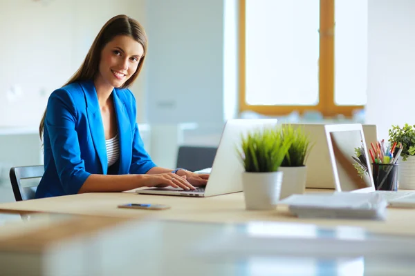 Kobieta siedząca na biurku z laptopem. — Zdjęcie stockowe