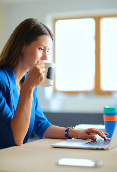 Bir fincan kahve tutan ofis masa başında oturan çekici gülümseyen iş kadın. — Stok fotoğraf