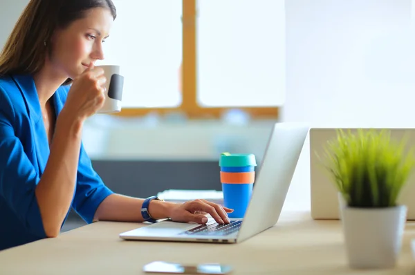 Mulher de negócios sorrindo atraente sentado na mesa do escritório, segurando uma xícara de café . — Fotografia de Stock
