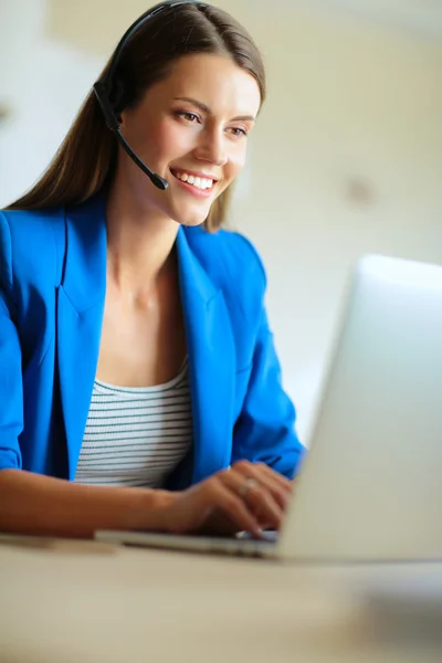 Porträtt av vacker affärskvinna som arbetar vid sitt skrivbord med headset och laptop.. — Stockfoto