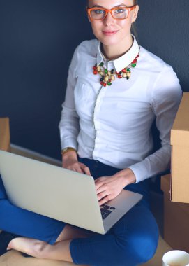 Kadın yerde dizüstü bilgisayarlı bir kutunun yanında oturuyor.