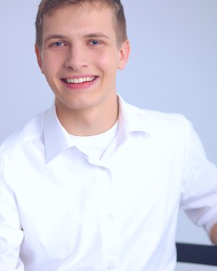 Gri arka plan üzerinde oturan gülümseyen genç adam portresi