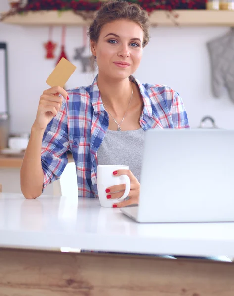 Mulher sorrindo compras on-line usando computador e cartão de crédito na cozinha — Fotografia de Stock