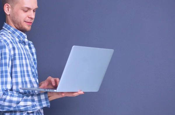 Portret van zelfverzekerde jonge man met laptop staan over grijze achtergrond — Stockfoto