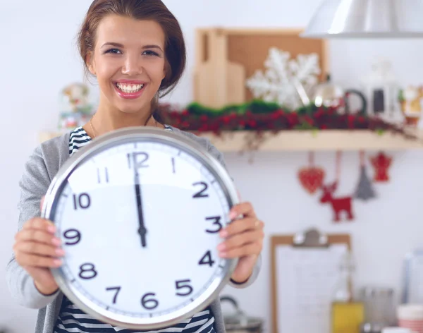 Glückliche junge Frau zeigt Uhr in weihnachtlich dekorierter Küche — Stockfoto