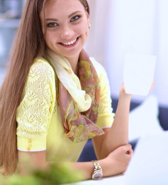 Elinde evrakları olan kadın masanın üstünde oturuyor.