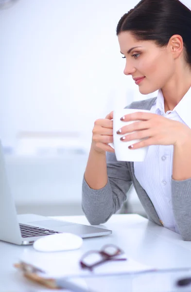 Jonge zakenvrouw zit op het bureau met beker in het kantoor — Stockfoto