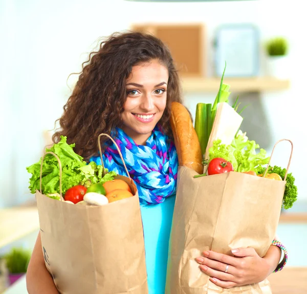 Mujer joven sosteniendo bolsa de la compra de comestibles con verduras de pie en la cocina. — Foto de Stock