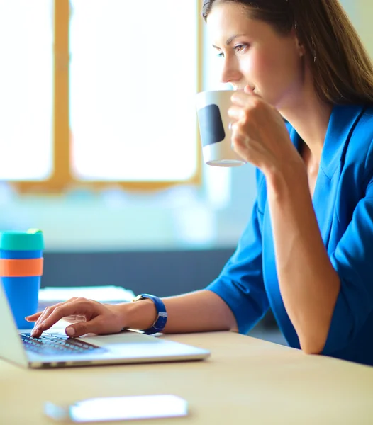 Wanita bisnis yang tersenyum menarik duduk di meja kantor sambil memegang secangkir kopi . — Stok Foto