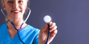 Steteskopla dinleyen kadın doktor, gri arka planda izole edilmiş.