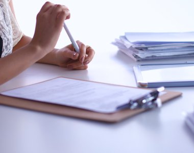 Elinde evrakları olan kadın masanın üstünde oturuyor.