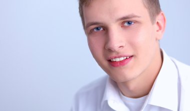 Gri arka plan üzerinde oturan gülümseyen genç adam portresi