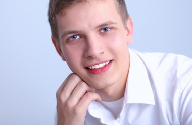 Gri arka plan üzerinde oturan gülümseyen genç adam portresi