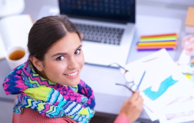 Ofis masasında çalışan genç, çekici bayan moda tasarımcısı, cep telefonuyla konuşurken çizim yapıyor.