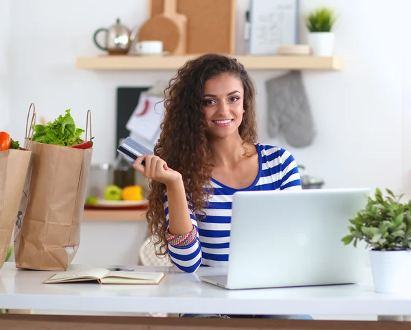 Leende ung kvinna med kaffekoppen och laptop i köket hemma — Stockfoto