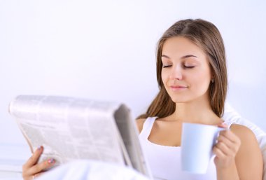 Genç ve güzel bir kadın yatakta gazete okuyan ve bir fincan çay keyfi