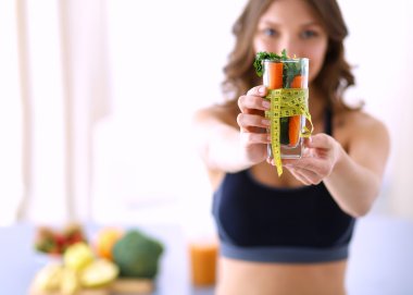 Elinde bir bardak dolusu taze meyve salatası ve bardağın etrafında mezura tutan bir kadın.