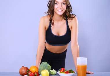 Sebzelerle masanın yanında duran genç ve güzel bir kadın.