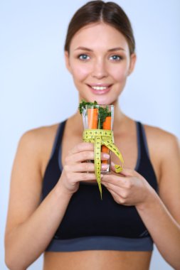 Elinde bir bardak dolusu taze meyve salatası ve bardağın etrafında mezura tutan bir kadın.