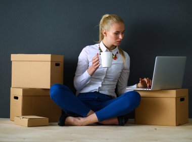 Kadın yerde dizüstü bilgisayarlı bir kutunun yanında oturuyor.