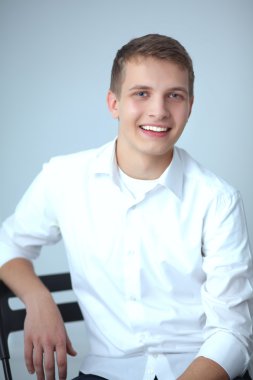 Gri arka plan üzerinde oturan gülümseyen genç adam portresi