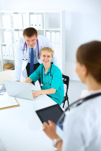 Bonito jovem sorridente médico feminino sentado na mesa — Fotografia de Stock