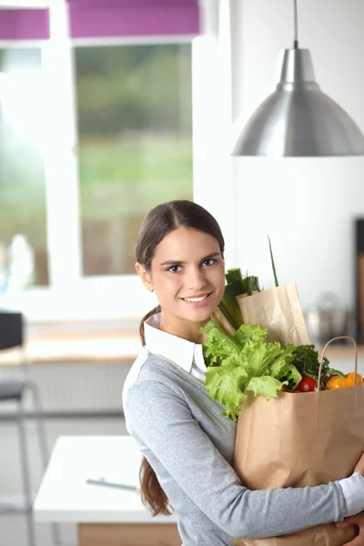 Giovane donna che tiene borsa della spesa con verdure. In piedi in cucina — Foto Stock