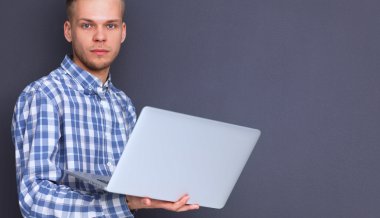 Gri arka plan üzerinde dizüstü bilgisayar konumu olan kendine güvenen genç adam portresi