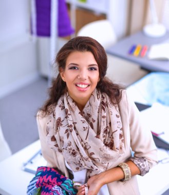 Gülümseyen kadın moda tasarımcısı ofis masasında oturuyor.