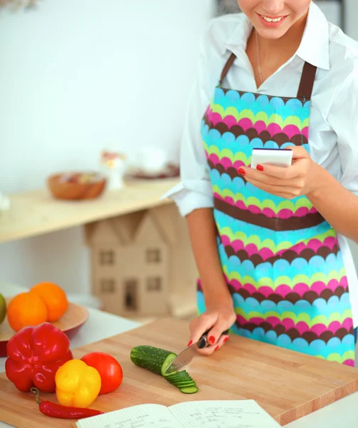 Mujer sonriente sosteniendo su teléfono celular en la cocina — Foto de Stock