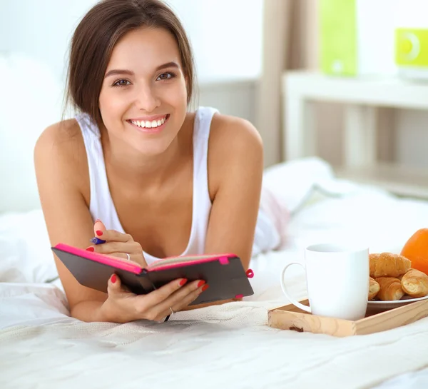 Jonge mooie vrouw zitten in bed en schrijven in een beurt — Stockfoto