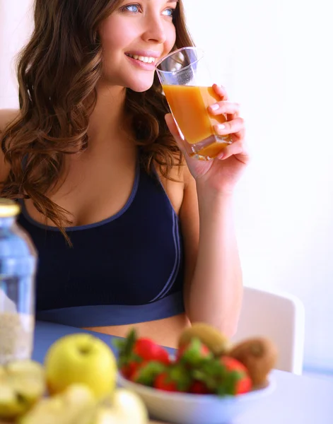 Chica sentada en la cocina en el escritorio con frutas y vasos con jugo —  Fotos de Stock