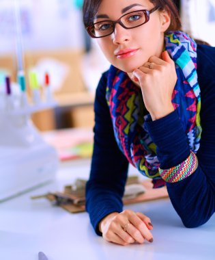 Güzel moda tasarımcısı stüdyoda masada oturuyor.